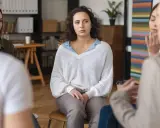 Kobieta z kręconymi włosami siedzi w kręgu, jej wyraz twarzy sugeruje zmaganie się z objawami OCD.
