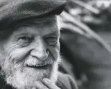 Un anziano con barba e berretto, il suo sorriso saggio evoca il significato che la morte si sconta vivendo appieno ogni istante.