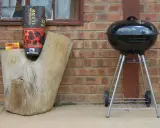 Grill stoi w bezpiecznej odległości od budynku, obok drewnianego pnia z węglem.