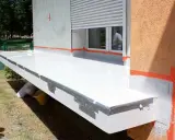 Balkon w trakcie prac wykończeniowych. Biała membrana hydroizolacyjna zabezpiecza płytę, pomarańczowa taśma uszczelnia krawędzie.