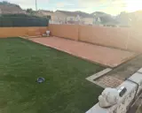 Un terrain de pétanque prêt pour l'entretien, avec une allée en gravier et une pelouse artificielle.