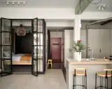 Une chambre en second jour, séparée par des portes vitrées. Une cuisine moderne avec un îlot et des tabourets complète l'espace.