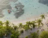 Rajska plaża na Gwadelupie Francuskiej. Ludzie kąpią się w turkusowej wodzie, łodzie kołyszą się przy brzegu, a palmy szumią nad piaszczystą plażą.