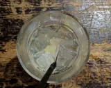 Ein Glas mit Eiswürfeln und einem schwarzen Strohhalm, bereit für einen erfrischenden Gin Tonic auf rustikalem Holztisch.