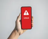 En hand håller upp en mobil med en röd skärm som varnar: "VIRUS".