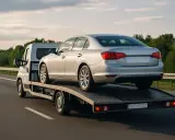 Srebrny samochód osobowy transportowany na lawecie po autostradzie.