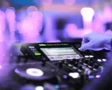 Mano su mixer, luci viola e rosa sfocate, creando l'atmosfera perfetta per la musica tech house.