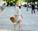 Kobieta w sukience w geometryczne wzory i espadrylach na koturnie idzie ulicą z brązową torebką.
