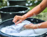 Manos lavando ropa blanca a mano en una tina con espuma, un método tradicional que explica qué significa lavado a mano en lavadora.
