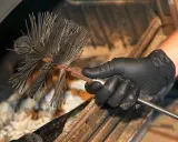 Main d'un ramoneur tenant une brosse pour cheminée. Le ramonage est essentiel pour l'assurance.