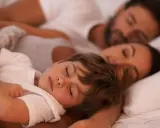 Ein kleiner Junge schläft friedlich im Arm seiner Eltern. Es ist schön, wenn das Kind jede Nacht ins Elternbett kuschelt.