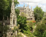 Sintra co zobaczyć: Quinta da Regaleira z wieżą i pałacem, otoczona bujną zielenią i kolorowymi rabatami.
