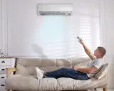 Hombre relajado en el sofá, ajustando el aire acondicionado para dormir cómodamente.