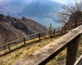 Sentiero con staccionata in legno per una passeggiata sul Pian dei Resinelli, con vista panoramica sul lago e le montagne.
