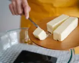 Ein Stück Butter wird mit einem Messer von einem Holzbrett gehoben, bereit für die Zubereitung von Butterschmalz.