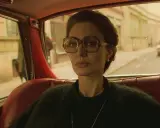 Angelina Jolie i en bil, en scen från en av hennes filmer. Hon bär stora glasögon och tittar ut genom fönstret.