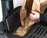 Persona rellena el depósito de una estufa de pellets con combustible.