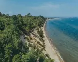 Malownicza plaża Mechelinki z zielonymi klifami i turkusowym morzem. Kilka osób odpoczywa na piasku, inni kąpią się w wodzie.