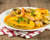 Plato de comida asturiana con un trozo de pescado, gambas y almejas en salsa.