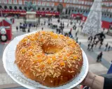 El mejor roscón de Madrid, adornado con almendras y fruta confitada, se presenta en la Plaza Mayor, un festín visual y delicioso.