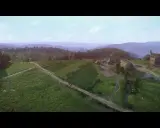 Krajobraz z gry Kingdom Come: Deliverance. Wiatrak i zabudowania na wzgórzu, pola uprawne i lasy w tle.