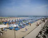 Spiaggia affollata a Rimini Gatteo Mare, con file ordinate di ombrelloni e lettini blu e bianchi, bagnanti e un molo di roccia.