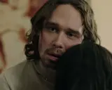 En man med långt hår och blå ögon kramar någon i tv-serien "Knutby".