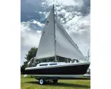Voilier Mac Gregor 25, prêt à naviguer, avec ses voiles blanches gonflées par le vent sous un ciel nuageux.