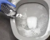 Guante azul vierte líquido de una botella en el inodoro. Solución para saber qué hacer si se atasca el vater.