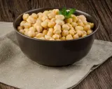 Schüssel mit Kichererbsen aus der Dose, bereit zum direkten Essen. Ein Hauch Petersilie und eine Knoblauchzehe im Hintergrund.