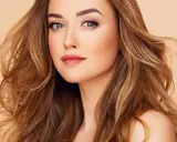 Mujer con cabello castaño dorado, ondulado y con reflejos claros. Su mirada es penetrante y sus labios pintados de rosa.