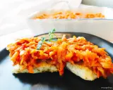 Ryba po grecku z marchewką i cebulą, udekorowana natką pietruszki. Pyszne danie na talerzu.