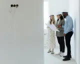 Tres arquitectos con cascos revisan planos en una obra, buscando cómo abaratar costes.
