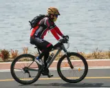 Rowerzysta w kasku i masce jedzie rowerem wzdłuż jeziora. Idealne noclegi dla rowerzystów czekają po wyczerpującej trasie.
