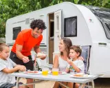 Familia disfrutando de un picnic en campamentos para familias, con una caravana de fondo.