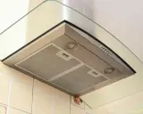 Nowoczesny okap kuchenny ze stali nierdzewnej i szkła, z filtrami i oświetleniem. Widoczne odprowadzenie okapu na zewnątrz przez ścianę.