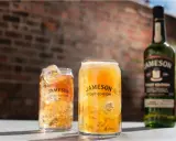Dwa orzeźwiające drinki z lodem i butelka Jameson Stout Edition na tle ceglanej ściany.
