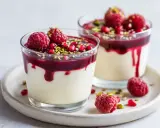 Två glas med krämig dessert, toppad med hallon, granatäppelkärnor och pistagenötter. Ett perfekt recept för en festlig avslutning.