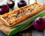 Tarta z karmelizowaną czerwoną cebulą, złocista i apetyczna, obok świeżych cebul i szczypiorku.