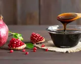 Granaty i gęsty, ciemny sos z granatów w miseczce i na drewnianej łyżce.