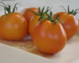 Cinq tomates orangées, comme des ananas noirs, reposent dans une caisse en bois.