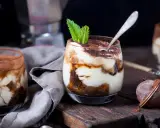Pyszne tiramisu w pucharkach, udekorowane listkiem mięty, na drewnianej desce.