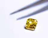 Un brillante giallo intenso, simile a un tesoro di **oro 18 carati**, attende di essere incastonato. Pinzette sfocate sullo sfondo.