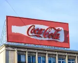 Duży baner logo Coca-Cola na dachu budynku, z charakterystyczną białą butelką i czerwonym napisem.