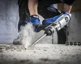 Ręce w rękawicach trzymają wiertarkę udarową, która kruszy beton. Dowiedz się, jak włączyć udar w wiertarce, by poradzić sobie z twardymi materiałami.