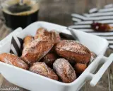 Beignets alsaciens schenkele dorés et saupoudrés de sucre, servis dans un plat blanc avec une tasse de café en arrière-plan.