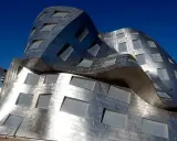 Edificio dalle forme ondulate e metalliche, una delle opere di Frank Gehry, con finestre quadrate e rettangolari.