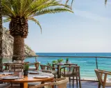 Mesas de restaurante con vistas al mar en el pola giverola resort, bajo palmeras.