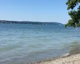 Sonniger Bodensee-Strand, ein echter Geheimtipp. Segelboote gleiten über das Wasser, während ein paar Schwimmer die Ruhe genießen.