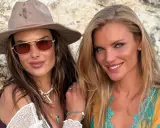 Alessandra Ambrosio y una amiga sonríen a la cámara, luciendo gafas de sol y joyas veraniegas.